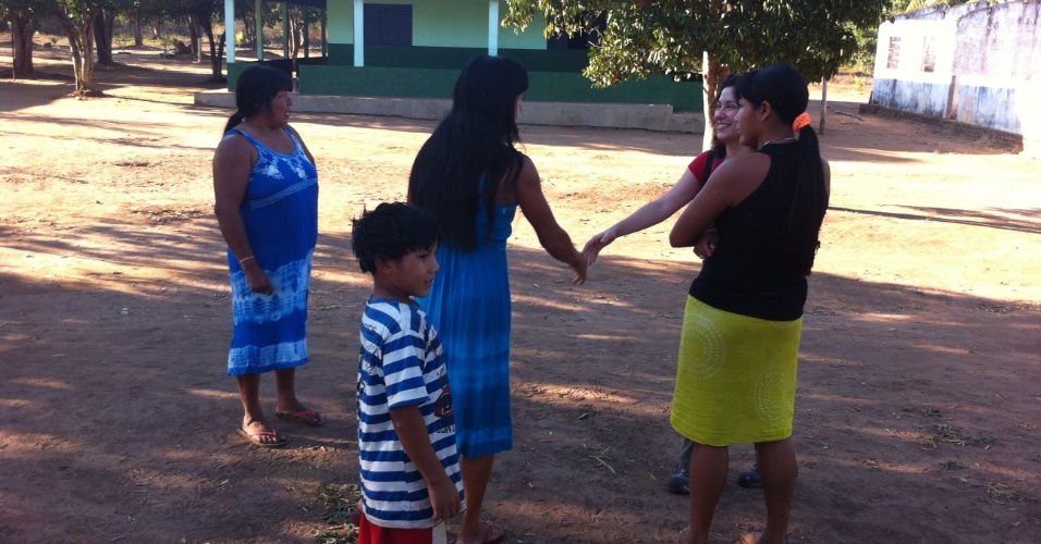 Gabriela Fujita (de vermelho), da equipe do UOL pelo Brasil, cumprimenta índias Kamaiurá, na aldeia Morená. Ao fundo o posto de saúde, um dos únicos dois prédios de alvenaria do local